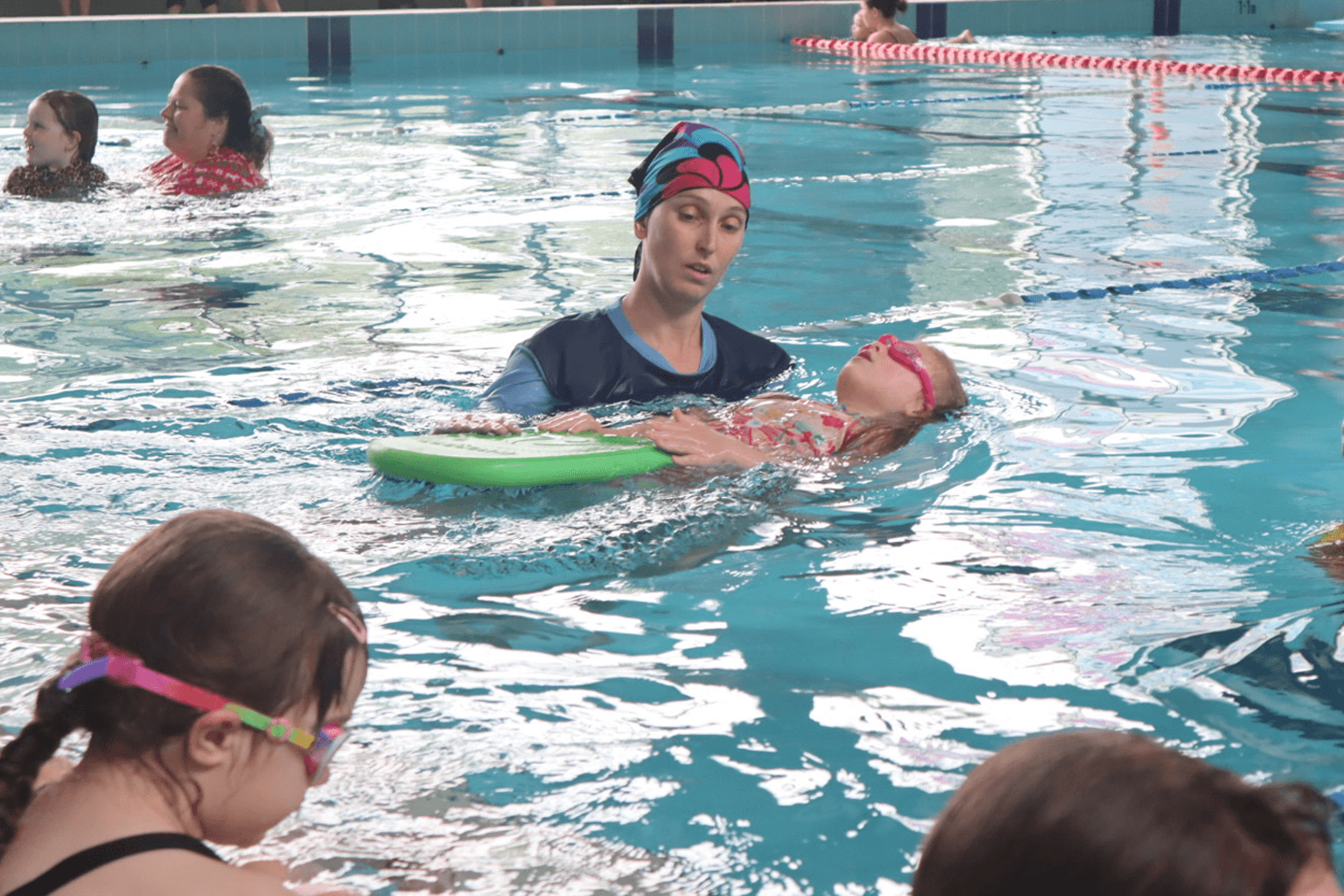 A swimming instructor in a pool helping a student float with a kickboard