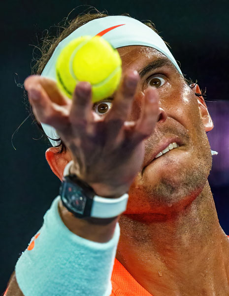 Close-up of tennis player Rafael Nadal holding a ball in front of his face, with his eyes visible through his fingers