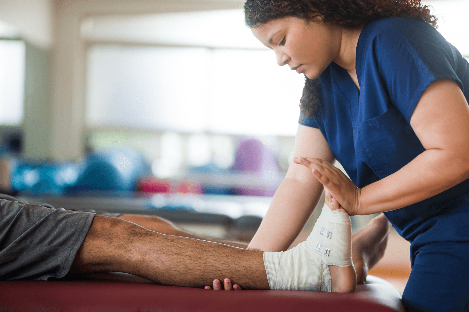 A woman medical professional helps a patient stretch a bandaged ankle.