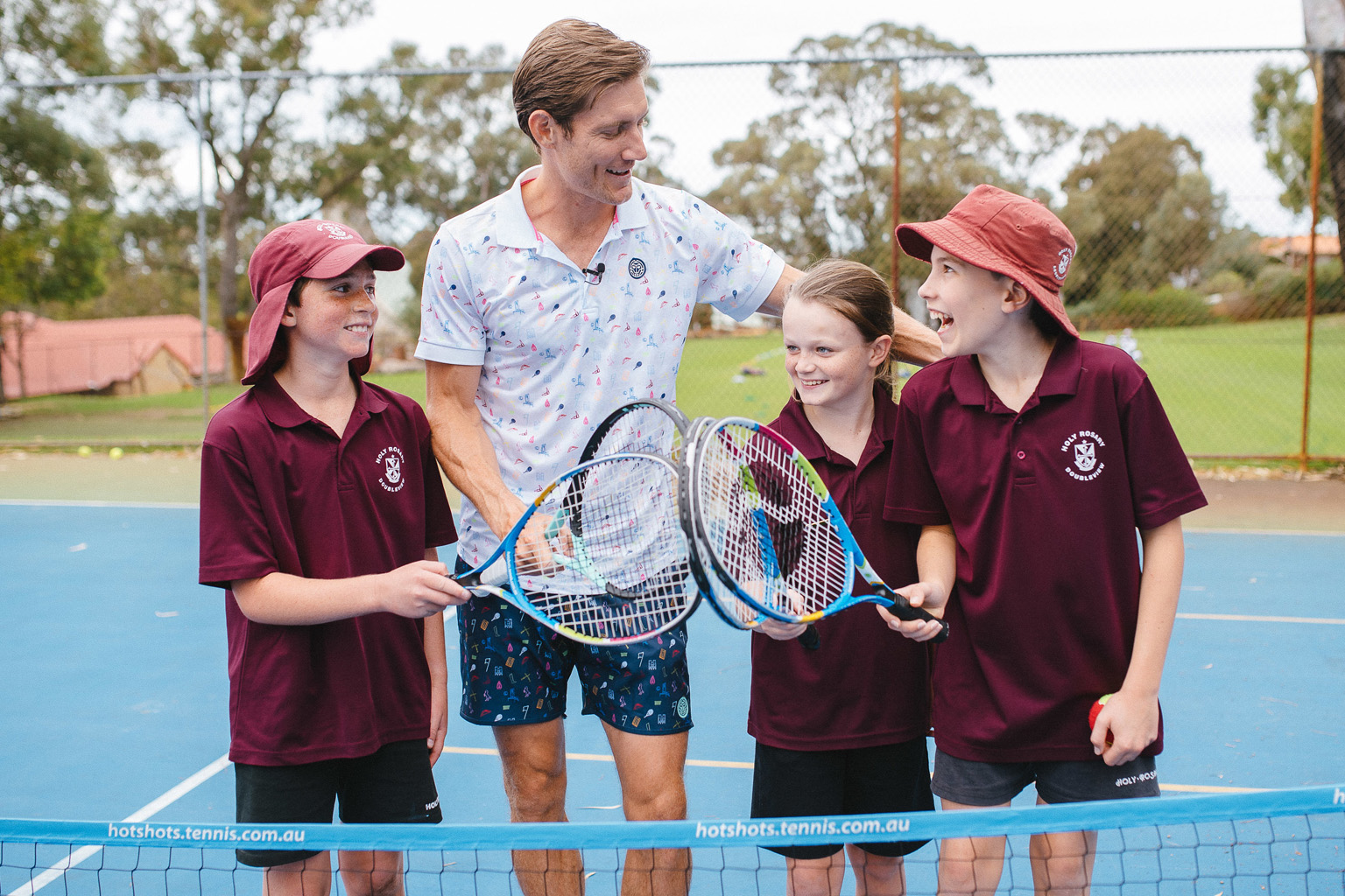 Tennis player Matt Ebden and school students stand together on a tennis court holding racquets.