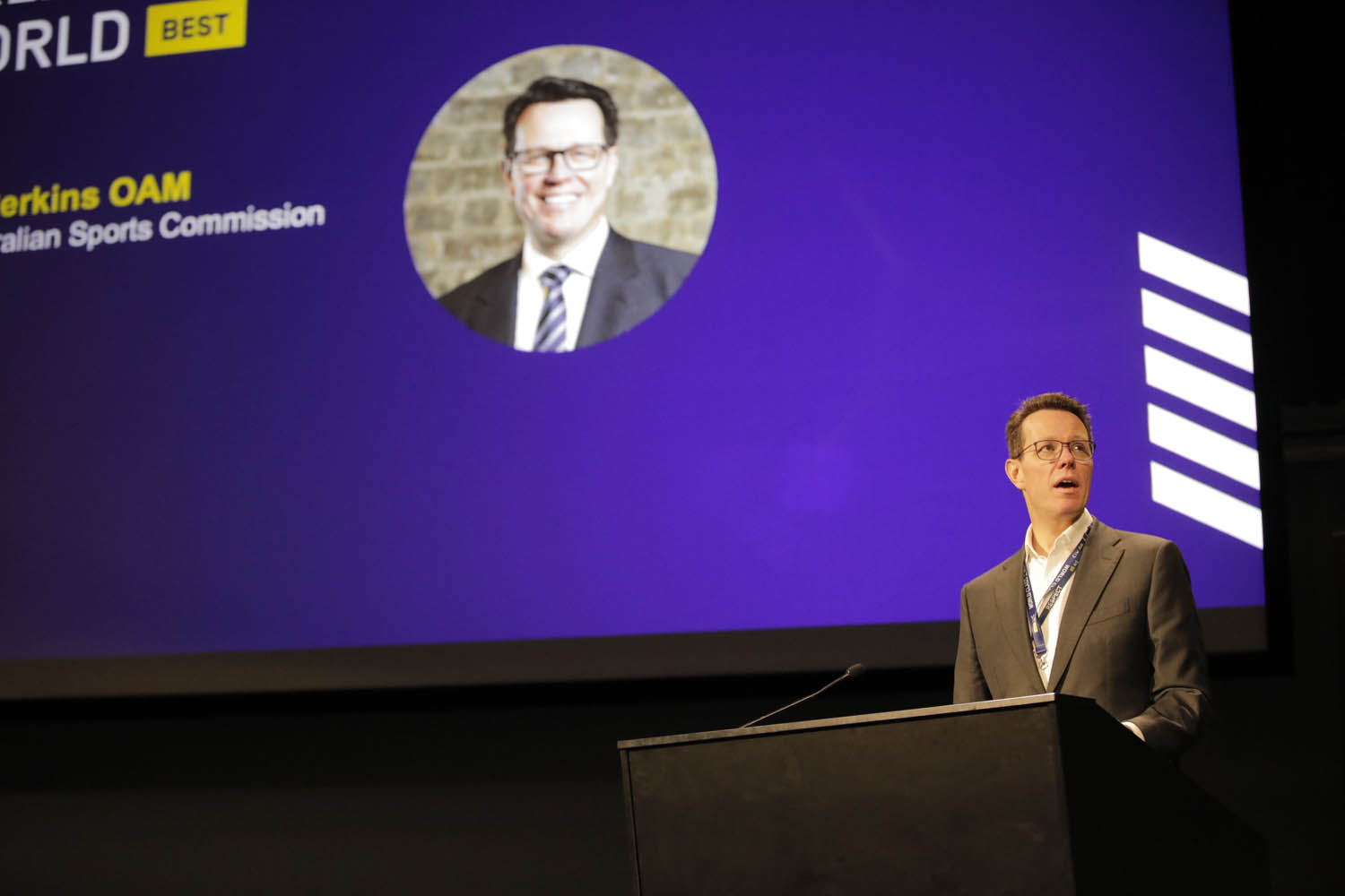 Kieren Perkins standing behind a lectern in front of a blue screen.