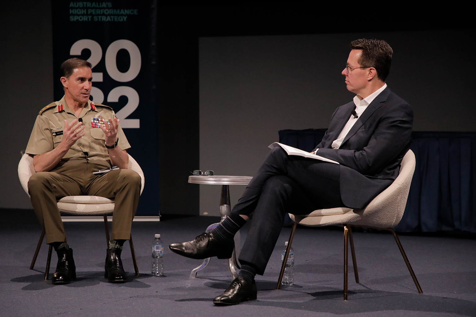 A man in military uniform speaks to a man in a suit