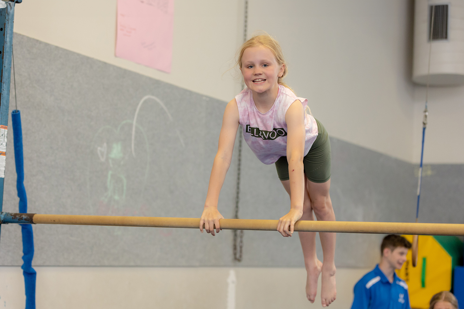A girl jumps in the air while holding a gymnastics bar