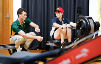 Olympic rower Alex Purnell helps Melba Copland Secondary School use a rowing machine.