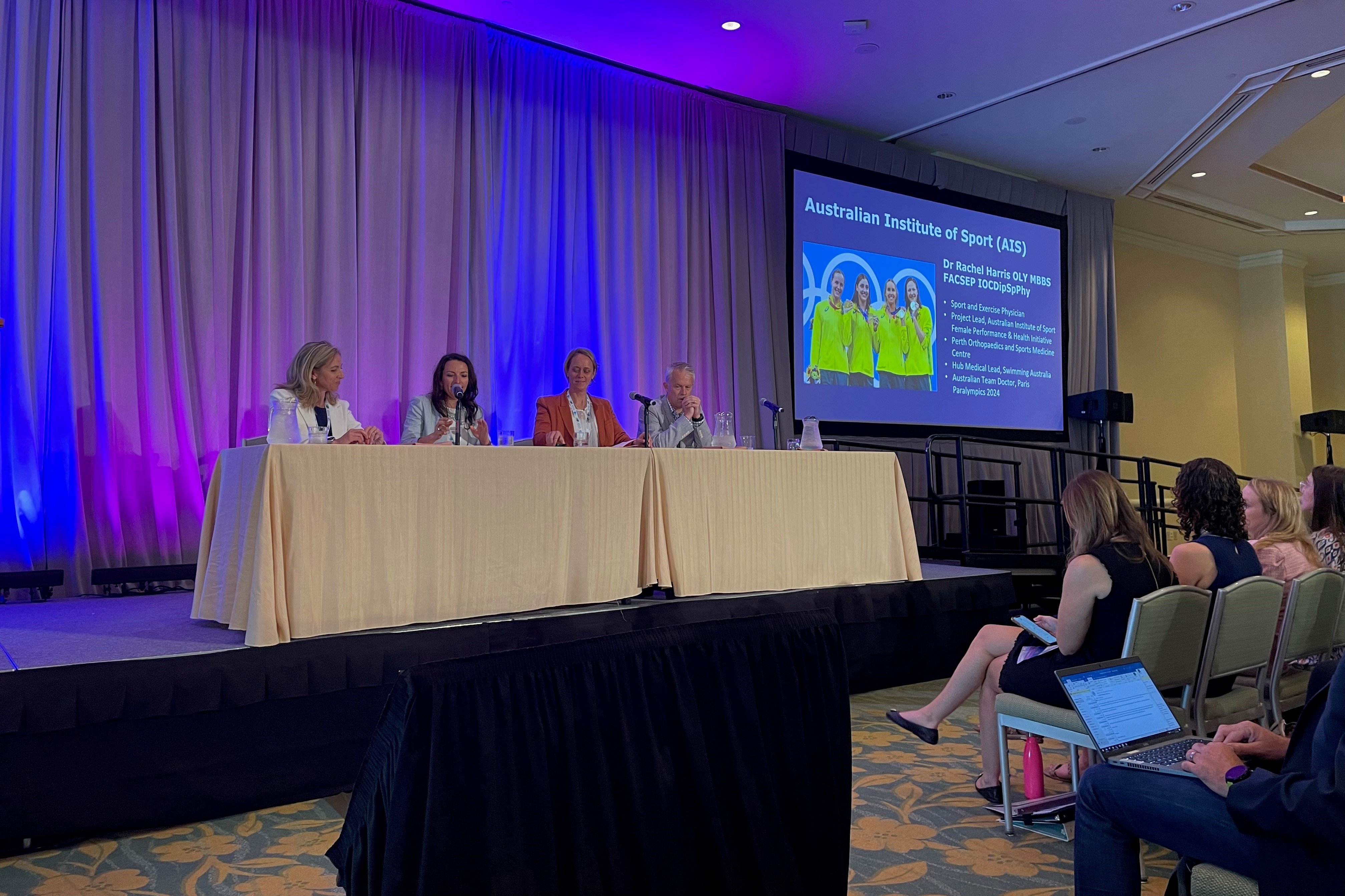 Panelists sit at table on stage.