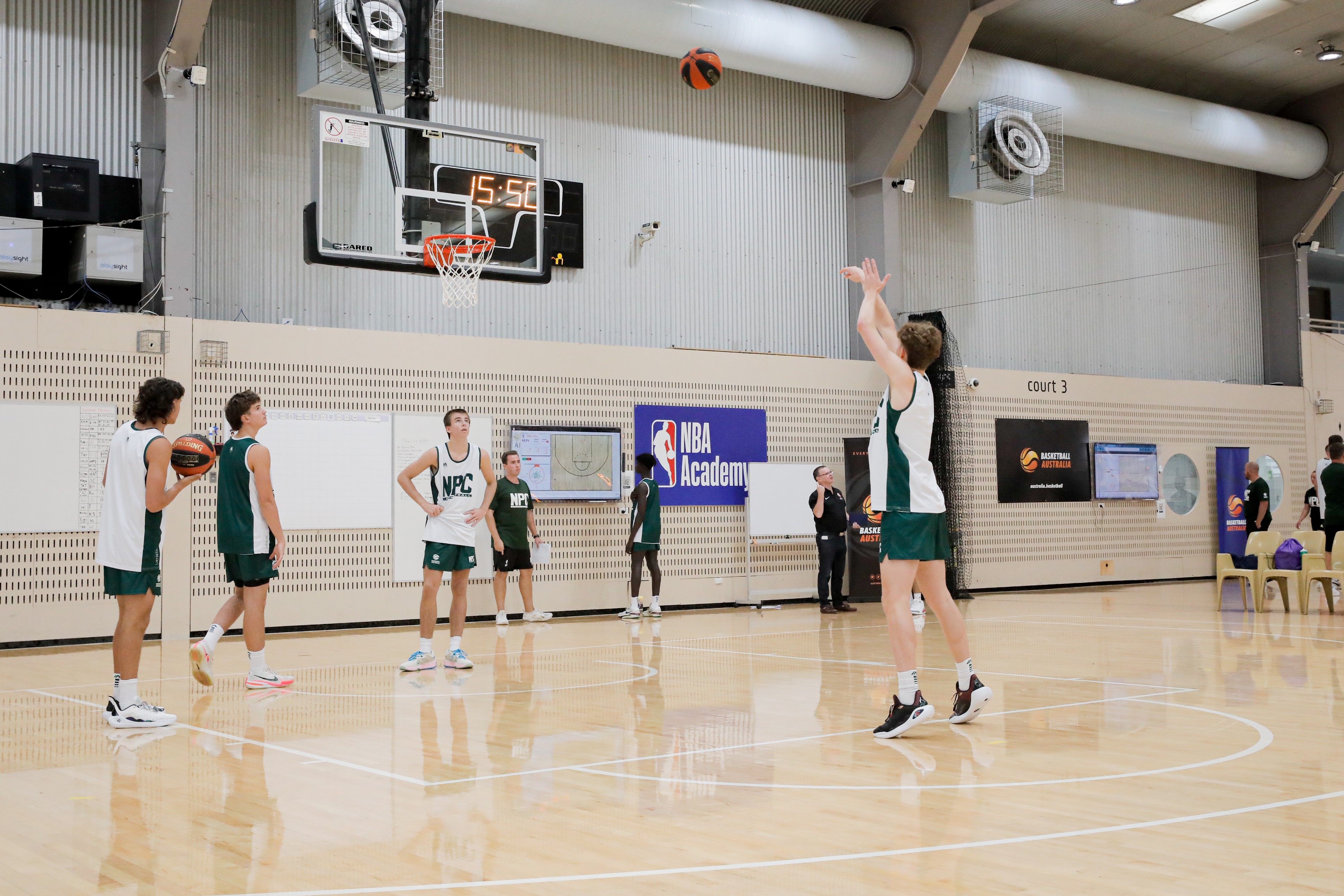 A group of young basketball athletes shooting a basketball into the hoop on the AIS basketball courts.
