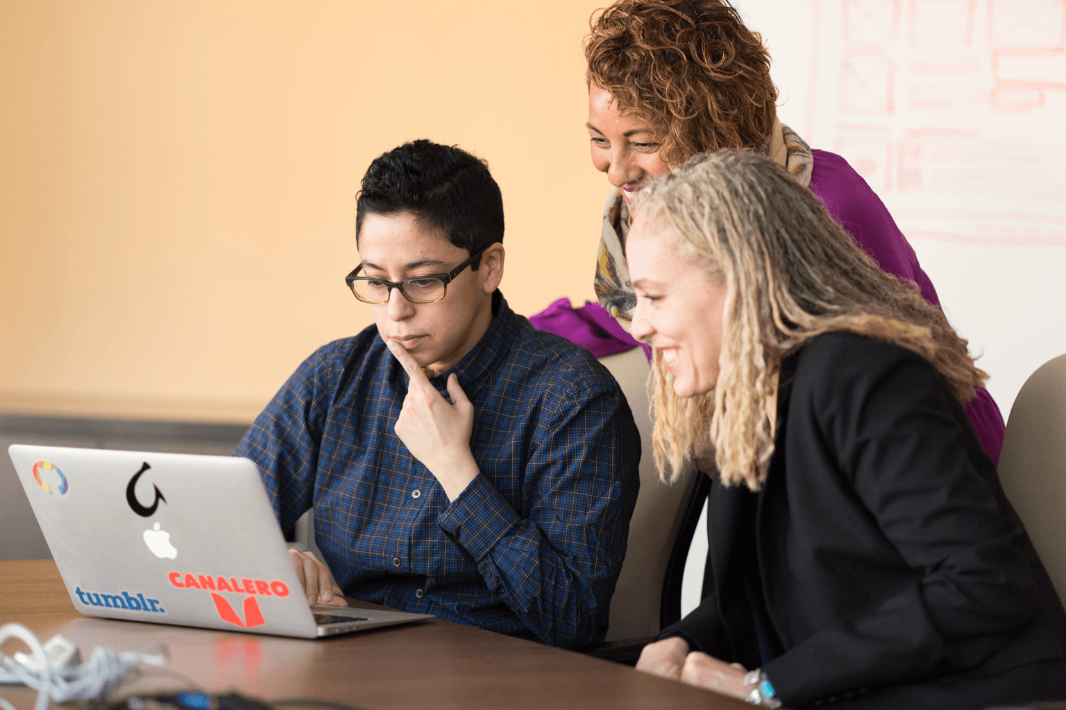 Three women sit together looking at a laptop screen