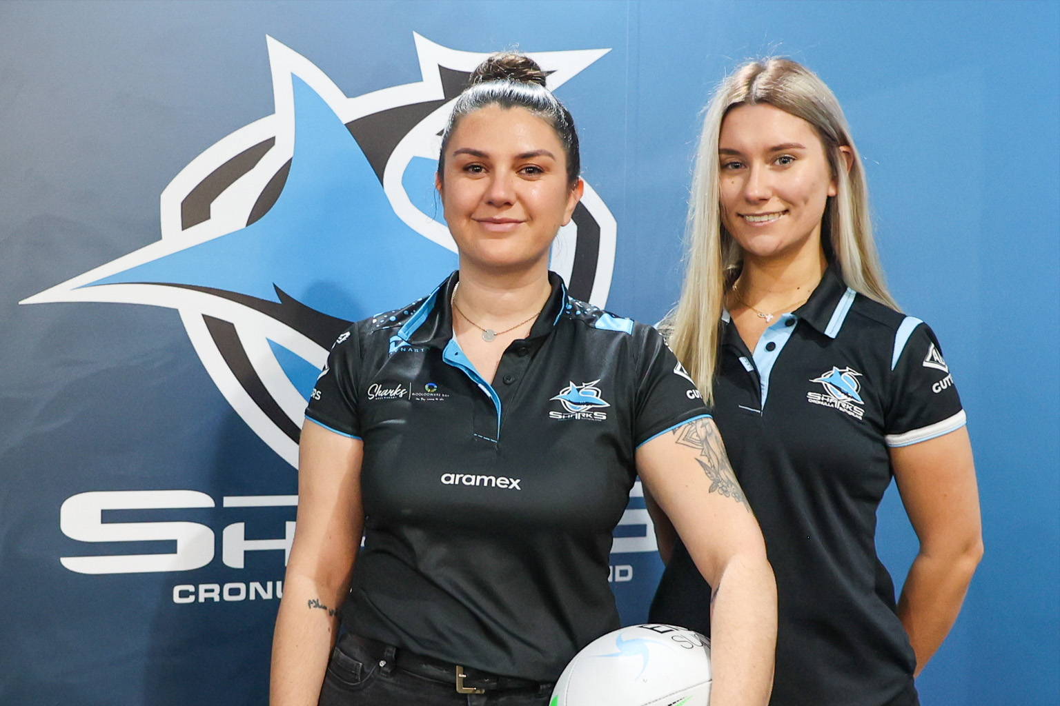 Rachal Allan and Julia Tzoukos stand in front of a Cronulla Sutherland Sharks logo