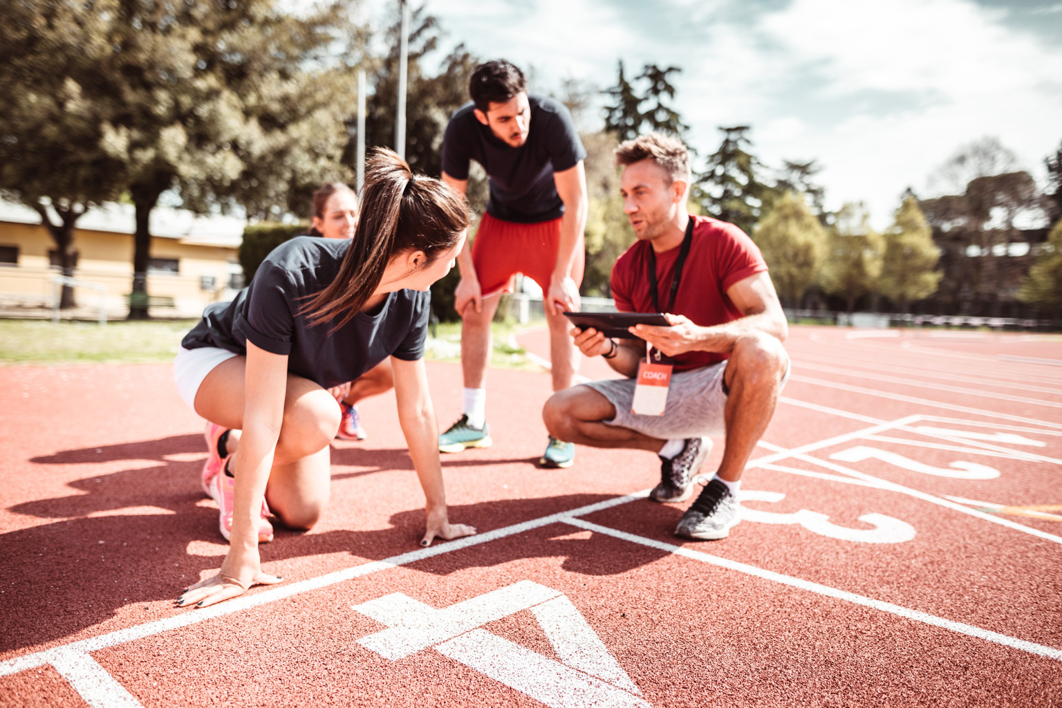 A coach holding an tablet computer speaks to athletes on a running track