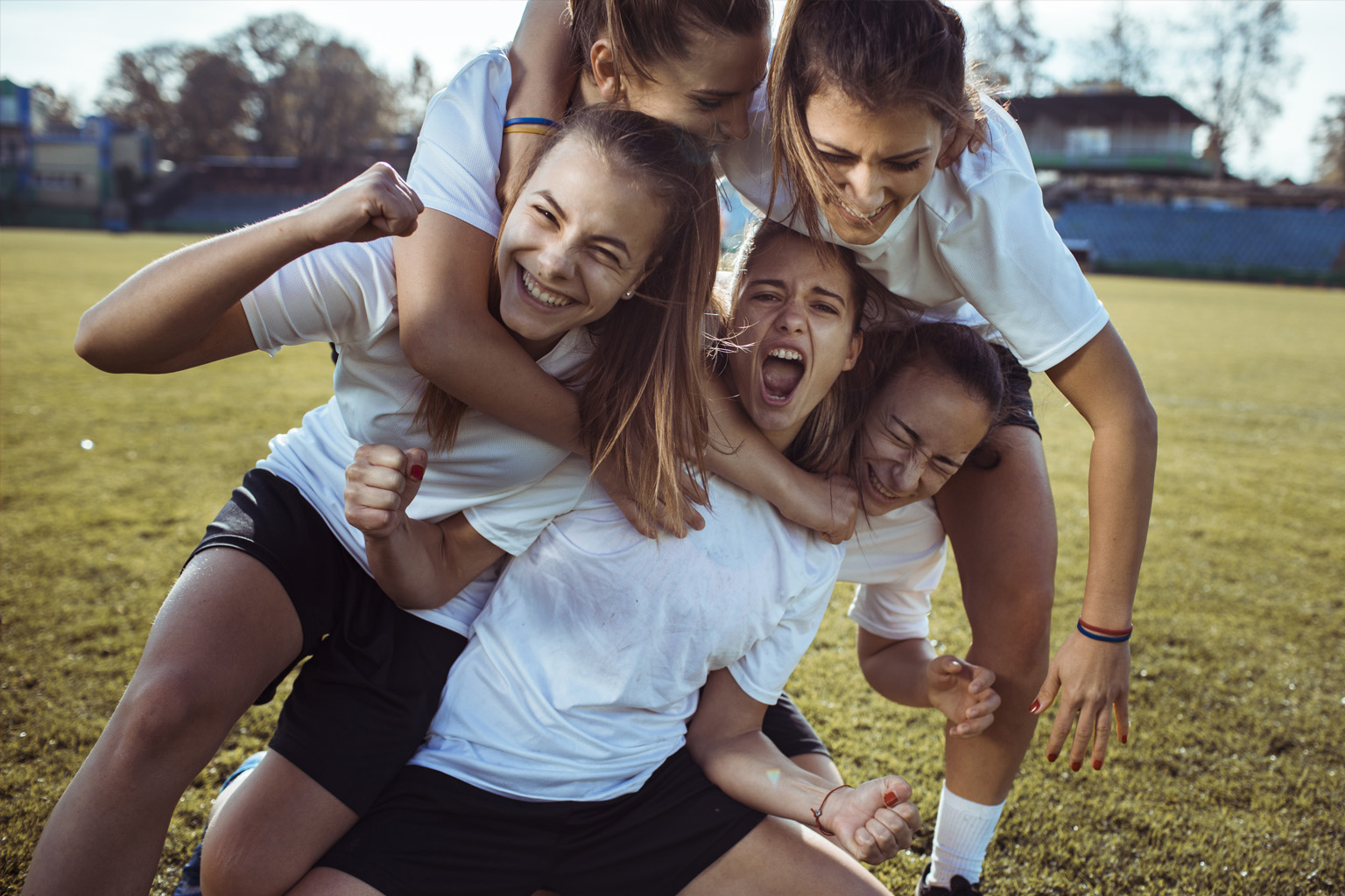 A group of young women crowd together in celebration on a sporting field.