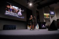 Wide image of a man on stage with a large projection screen in the background 