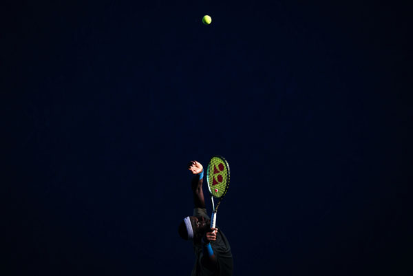 Tennis player Frances Tiafoe is lit by a narrow ray of sunshine while serving