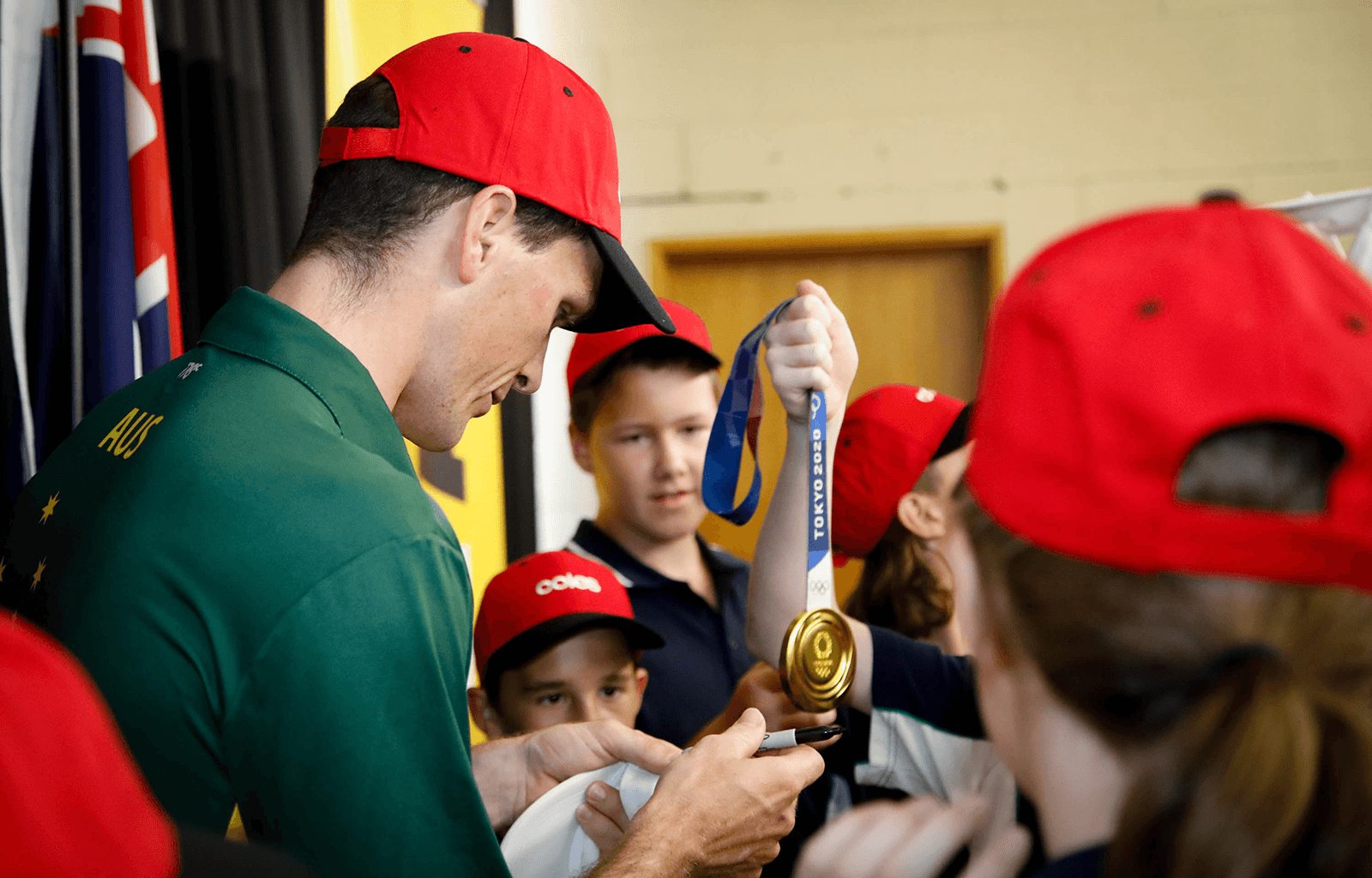 Alex Purnell's Olympic gold medal is held up in the middle of a group of students while he signs autographs.