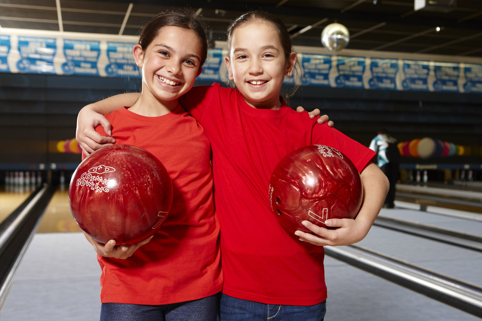Two girls holding bowling balls standing together at a tenpin bowling alley