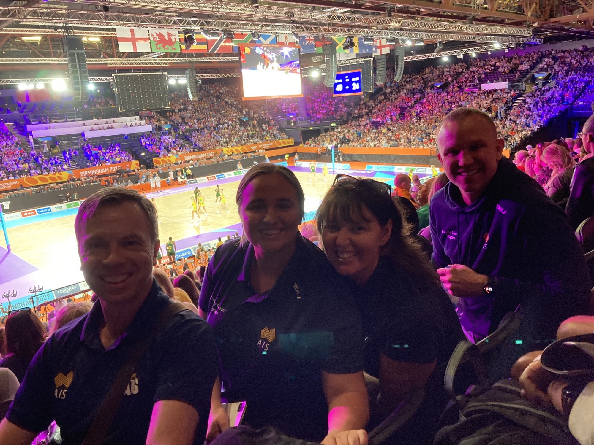 Coaches sit in the stands in front of a netball court