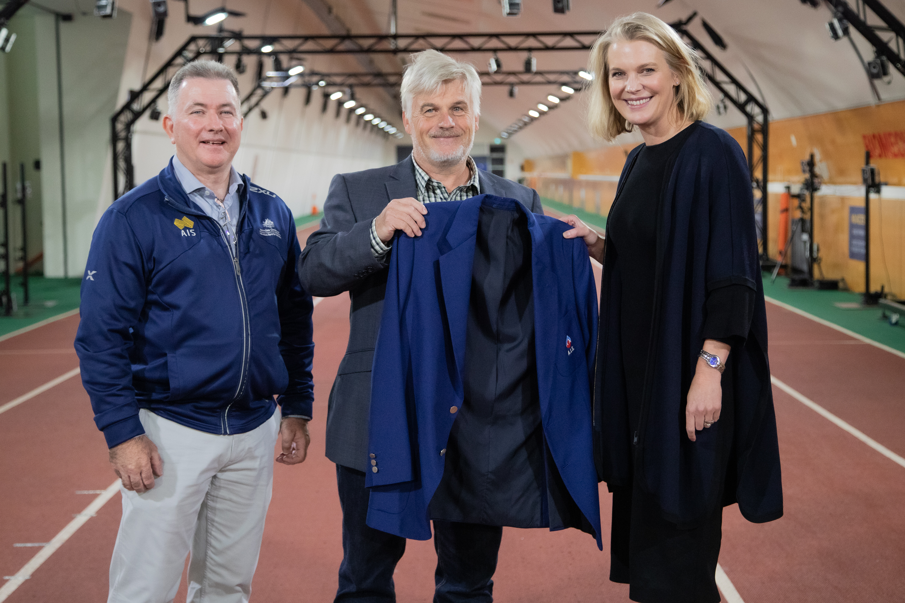 John Ellicott, son of AIS pioneer Bob Ellicott, presents AIS jacket to EGM of AIS Performance, Matti Clements, and AIS Performance Services Manager, Julian Jones.