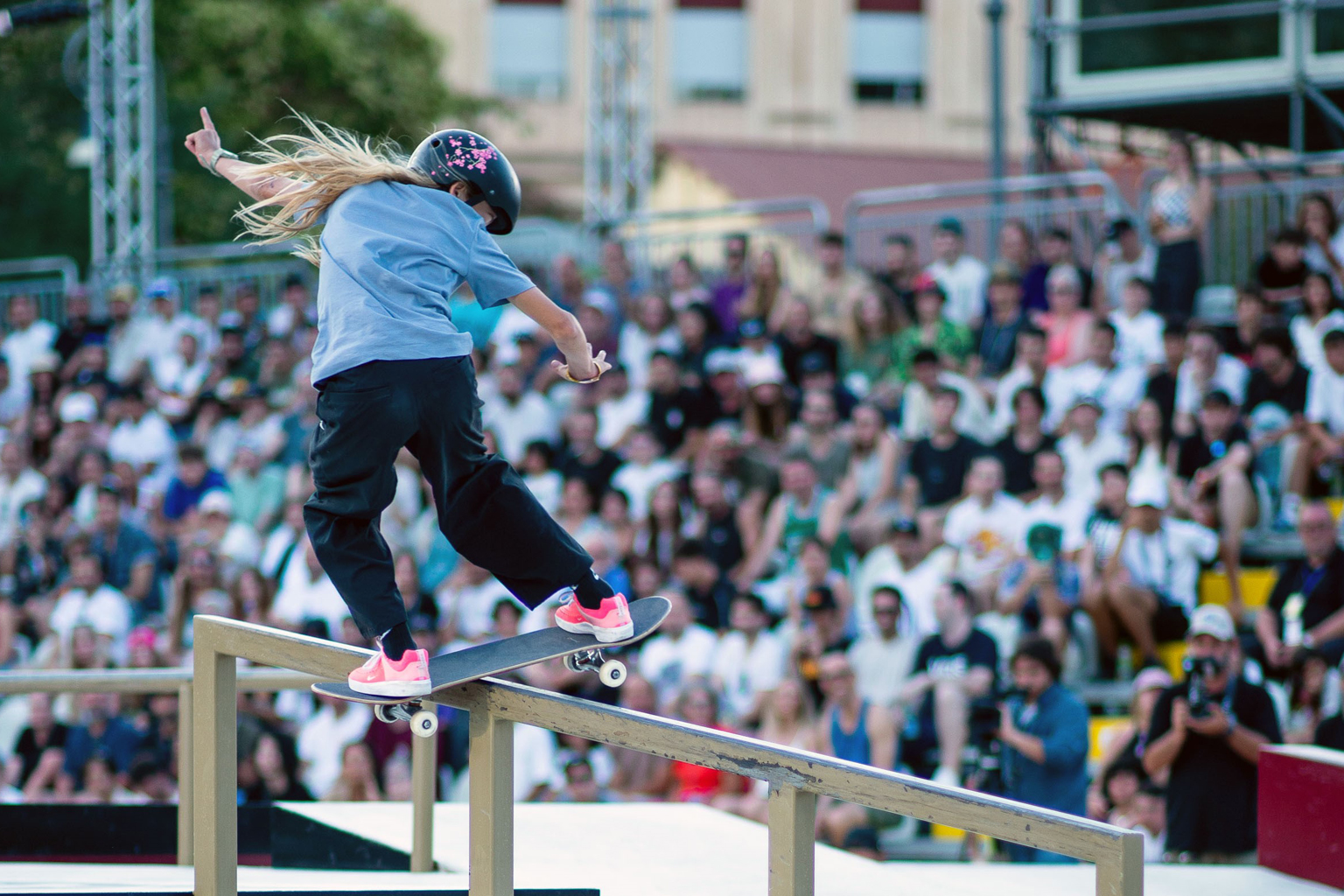 A girl slides down a rail on a skateboard in front of a large crowd