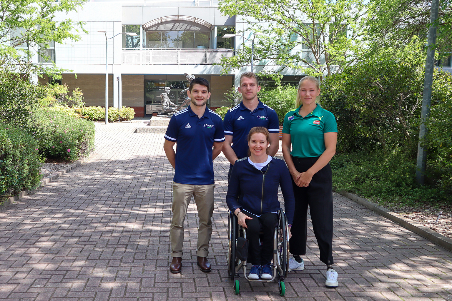 Three athletes standing and one athlete in a wheelchair gathered outside at the AIS.