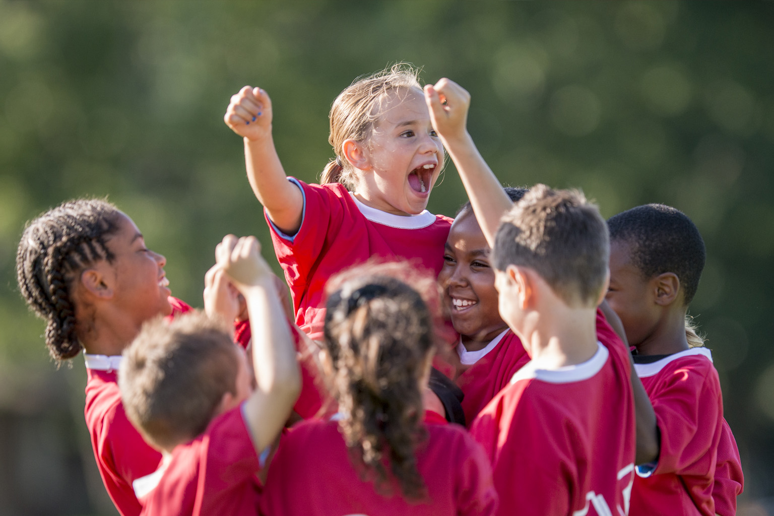 A small girl is lifted up by young teammates in celebration