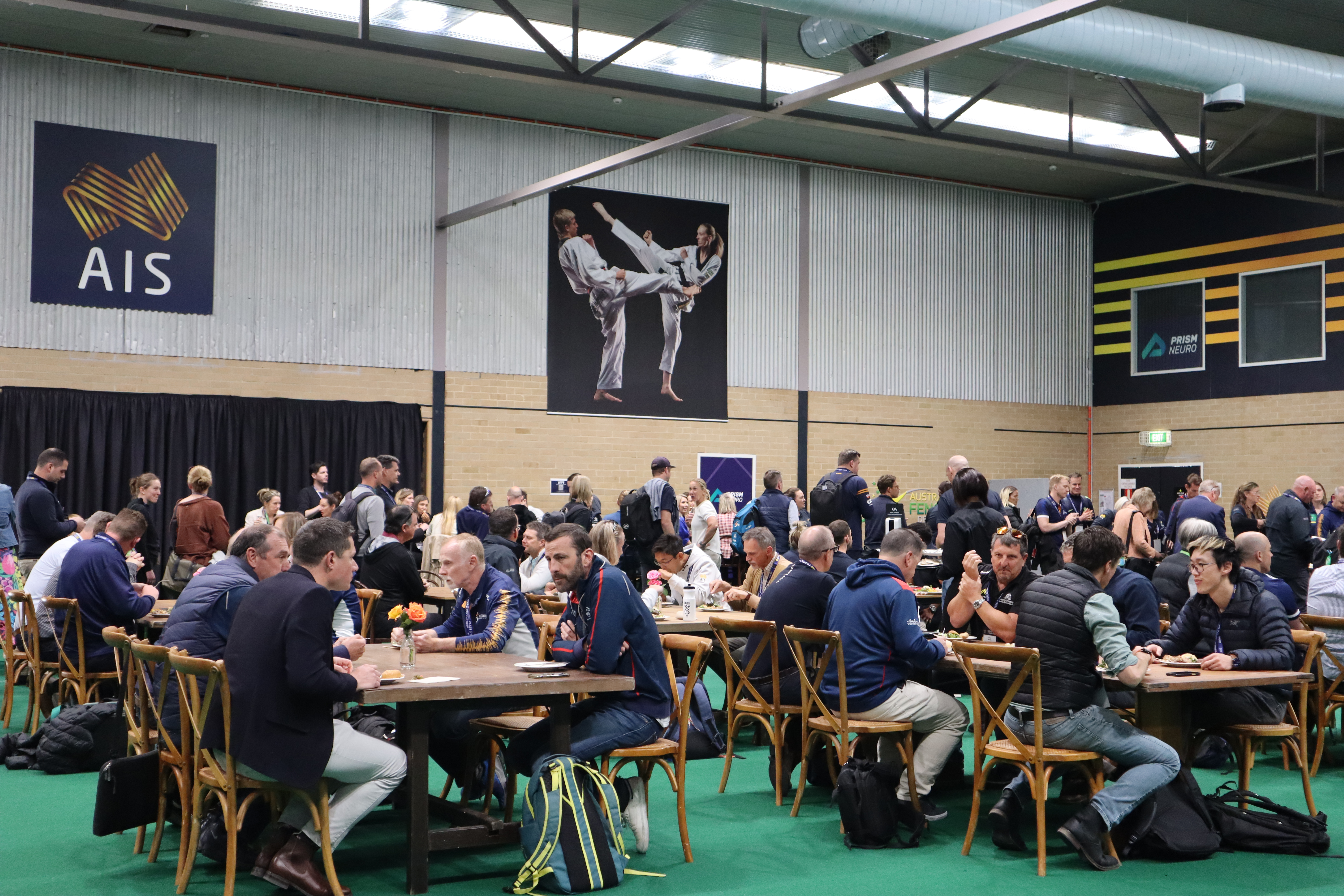 People seated at picnic-style tables inside the AIS Combat Centre