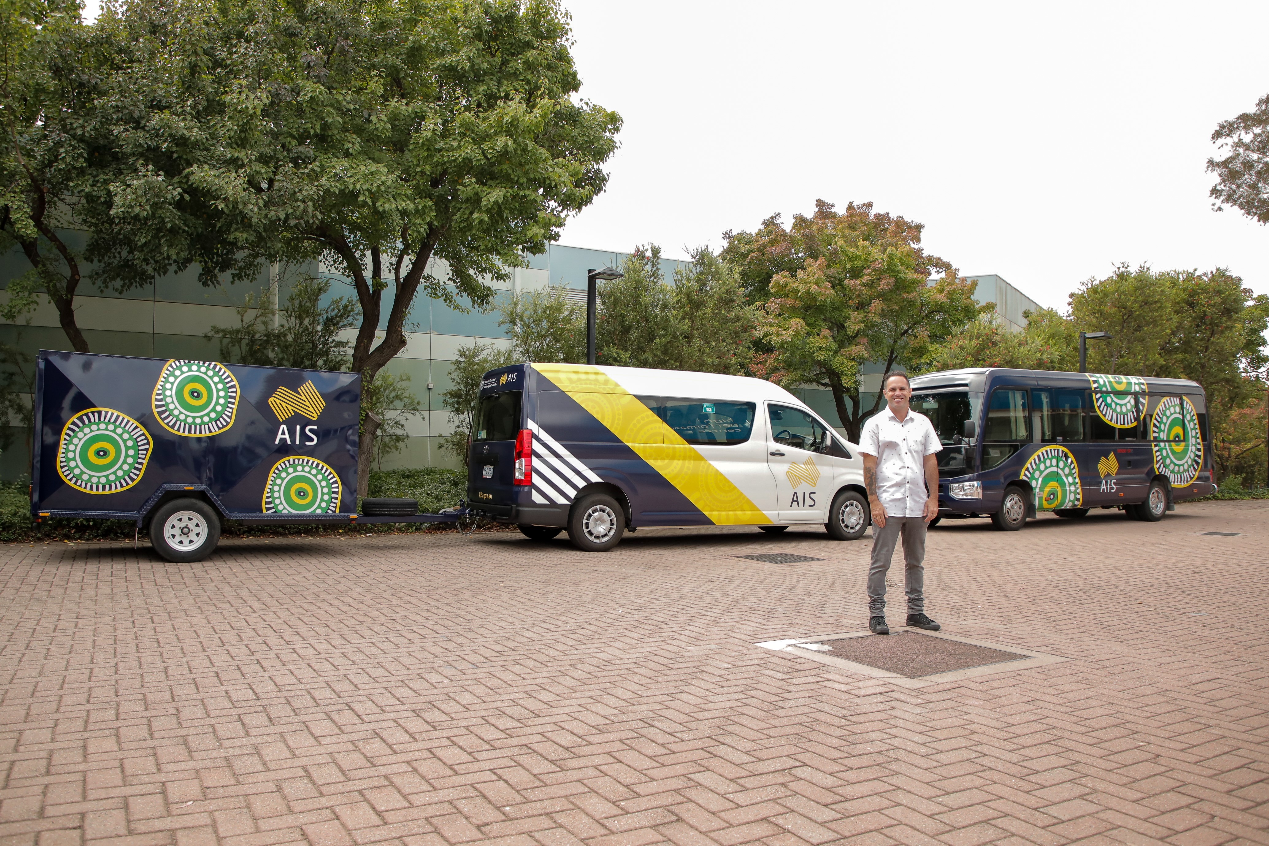 Artist Brad Hore pictured beside different AIS vehicles featuring his 'Kinship' artwork.