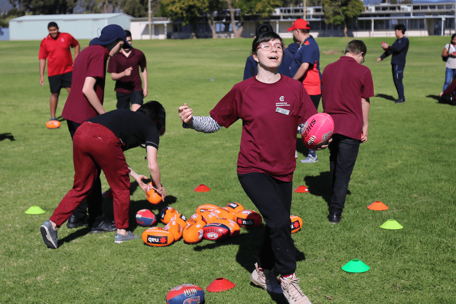 A school student runs with an Australian Rules football, with other students playing int the background