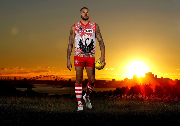 Buddy Franklin in Sydney Swans uniform stand before a sunset with Sydney Harbour Bridge in the background