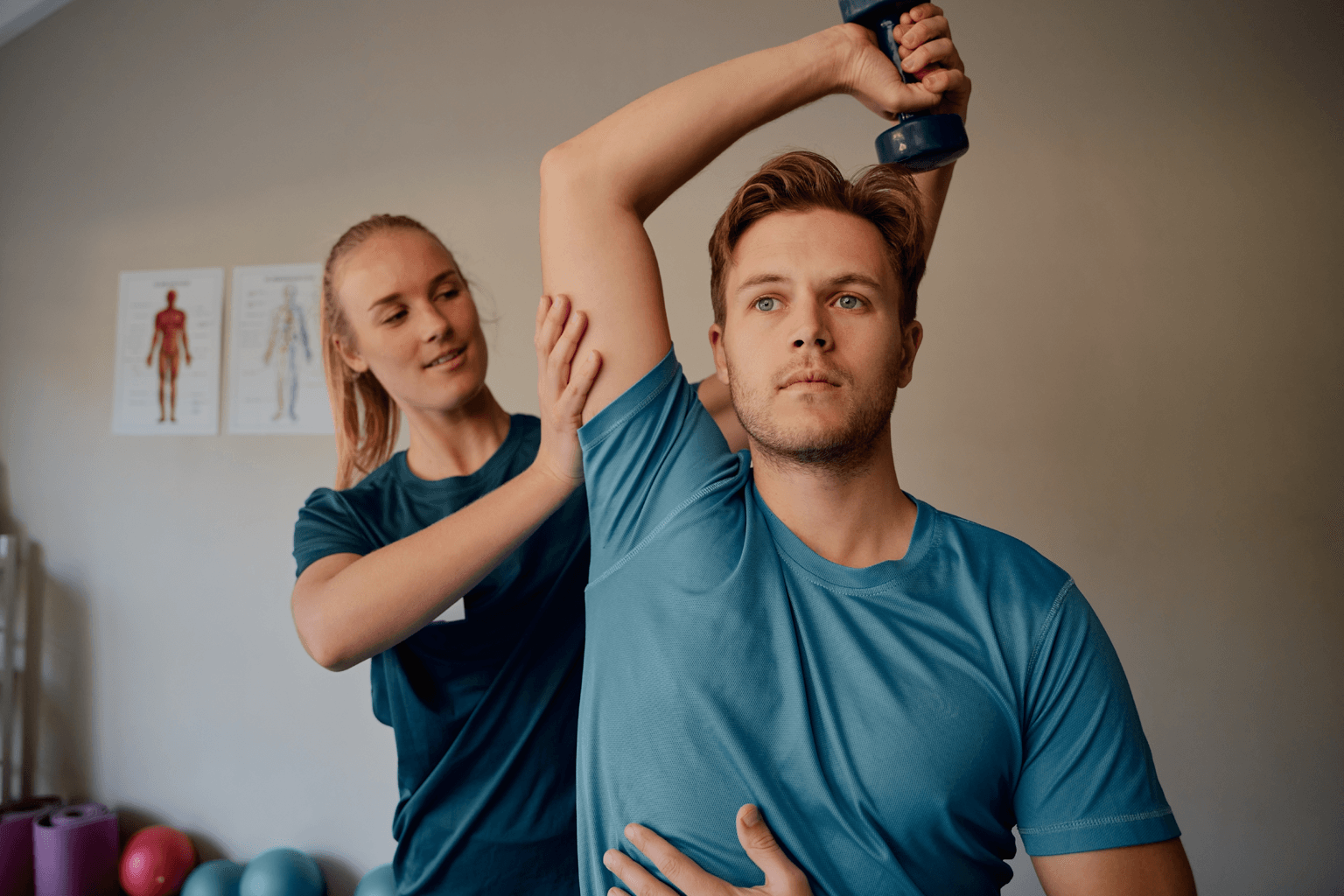A woman physiotherapist helps a patient raise his arm over his head while holding a handweight.