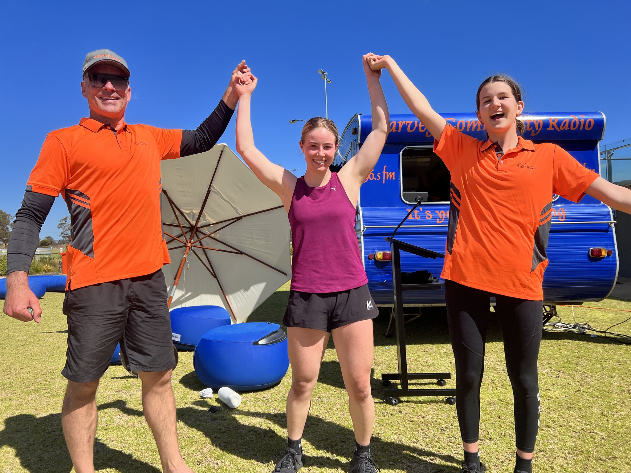 Three people stand together holding hands with their arms in the air.