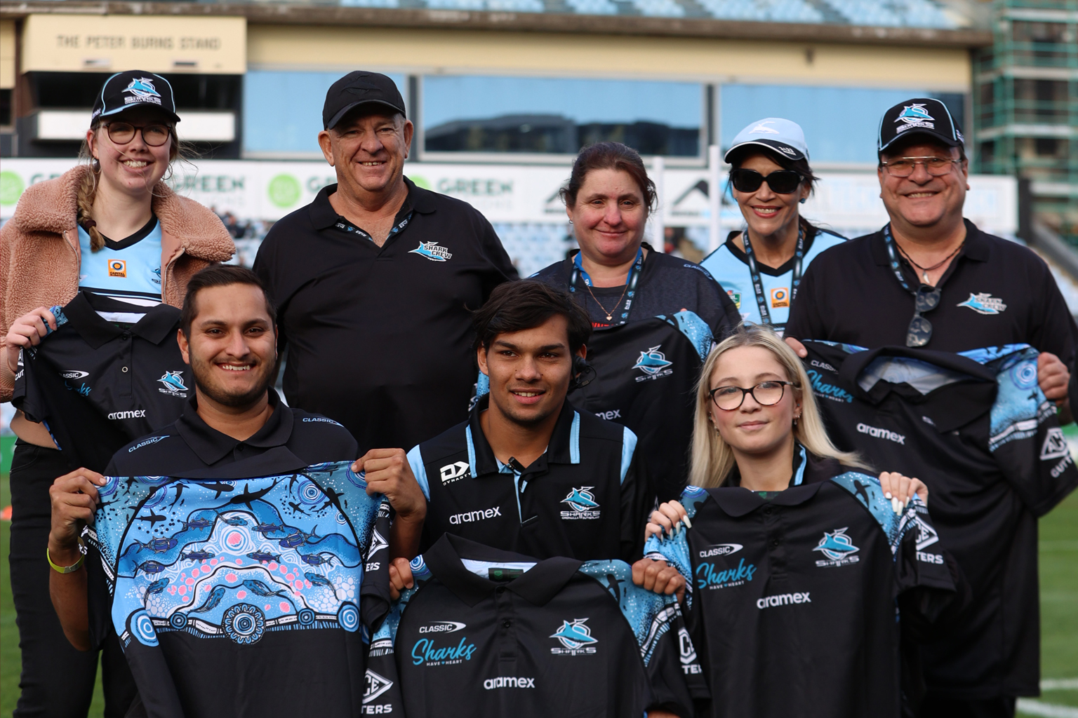 A group of people wearing Cronulla Southerland Sharks tops, holding up team merchandise.