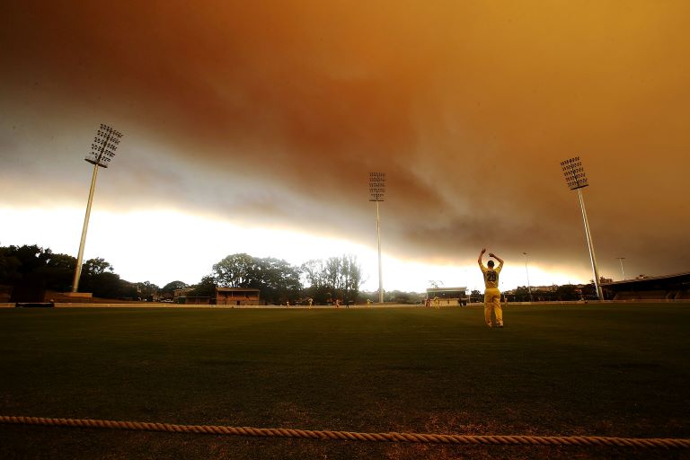 A cricket oval under an orange smoke haze.