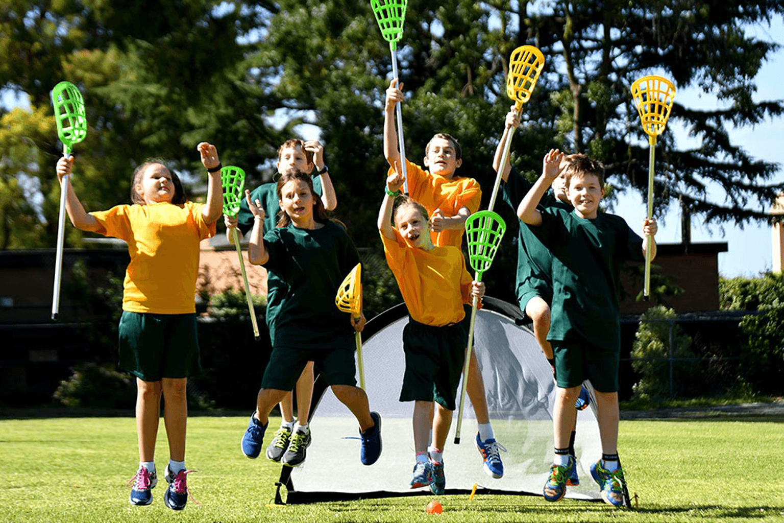 School children jumping on a grass field with lacrosse sticks 