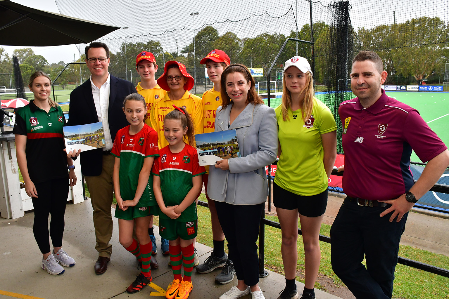 A group of AFL, cricket and surf lifesaving volunteers stand with Kieren Perkins and Anika Wells who hold copies of the Sport Volunteer Coalition Action Plan.