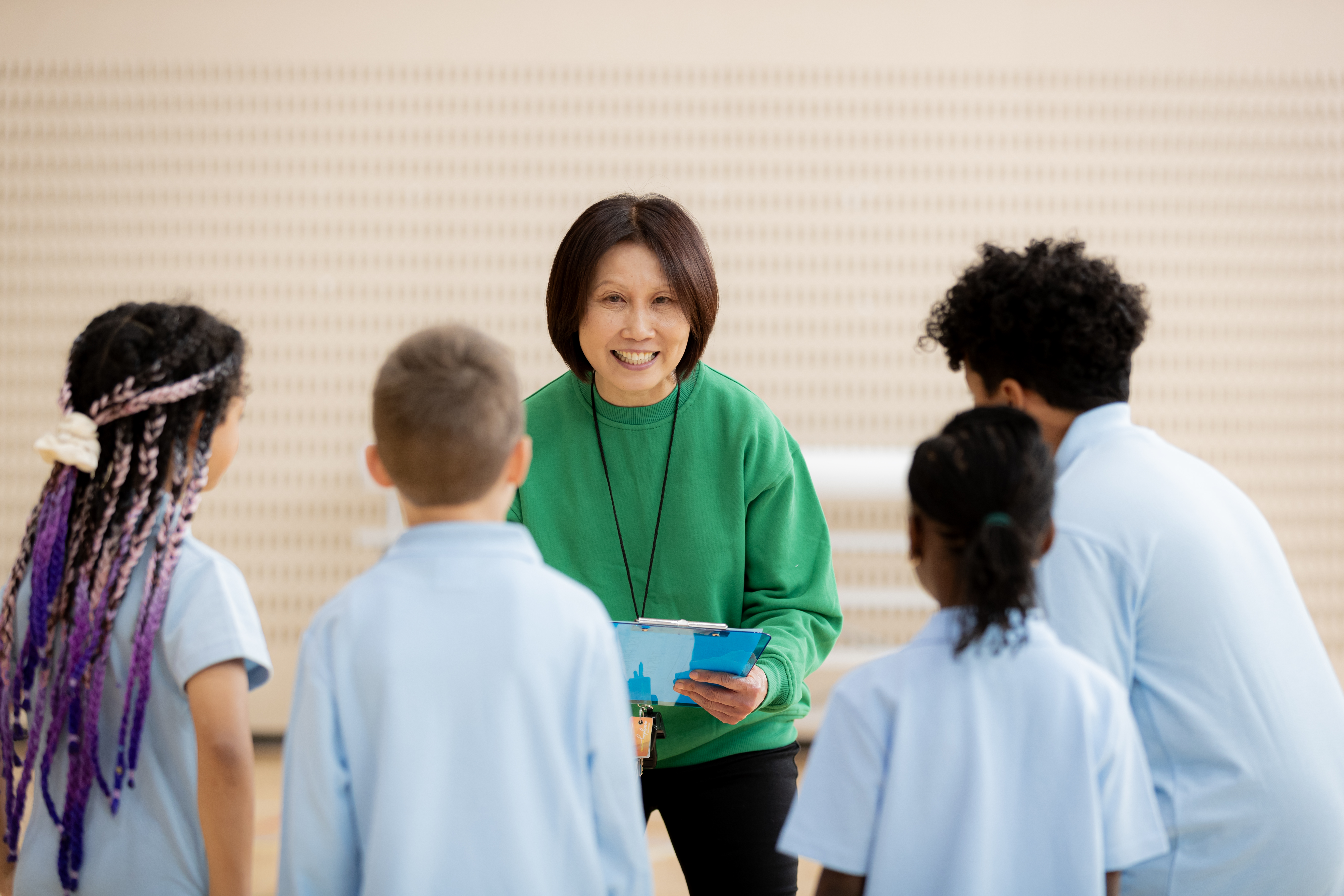 Lady stands facing camera holding whiteboard with kids watching her, back to camera.