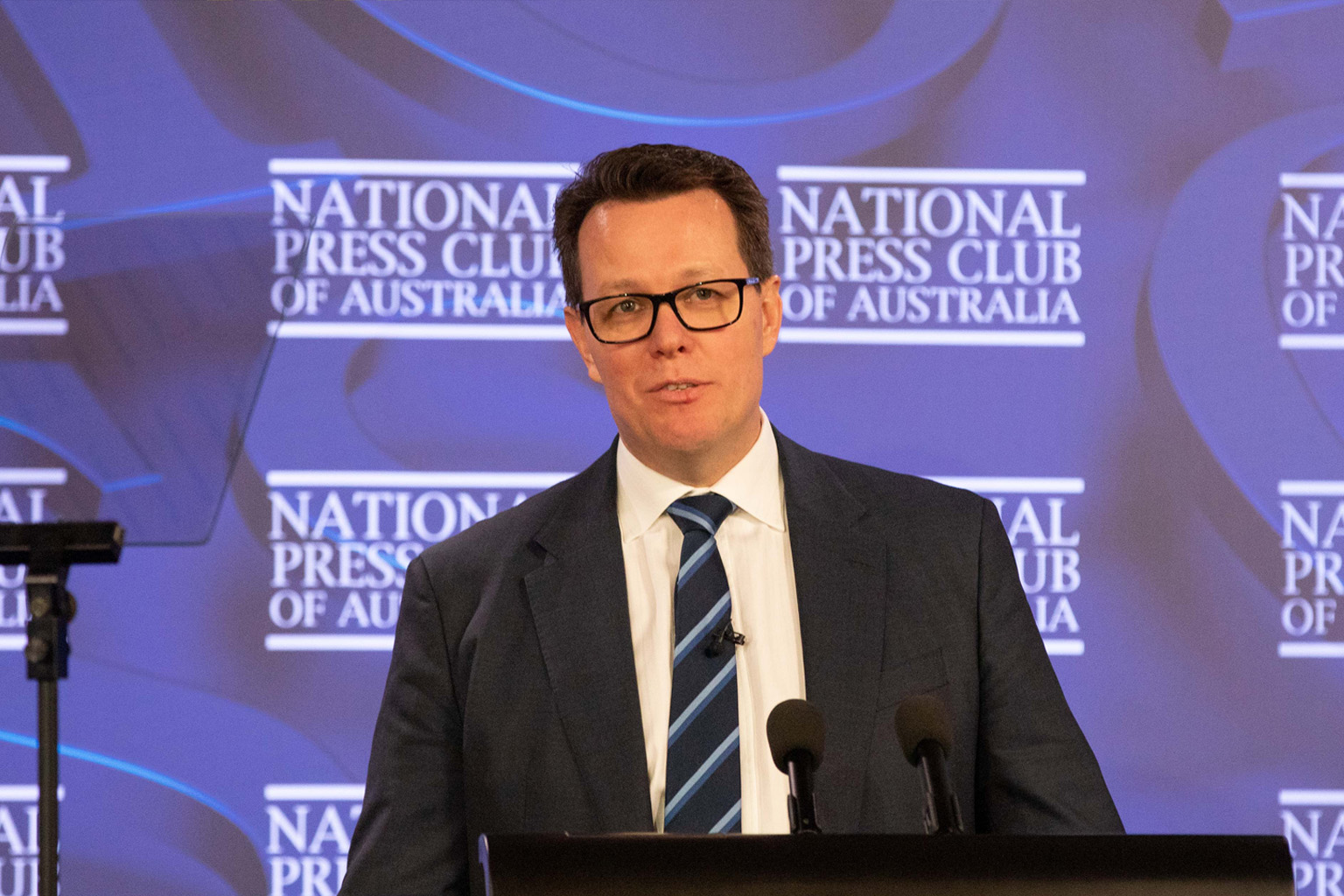 Kieren Perkins stands at a lectern in front of a naitonal press club backdrop