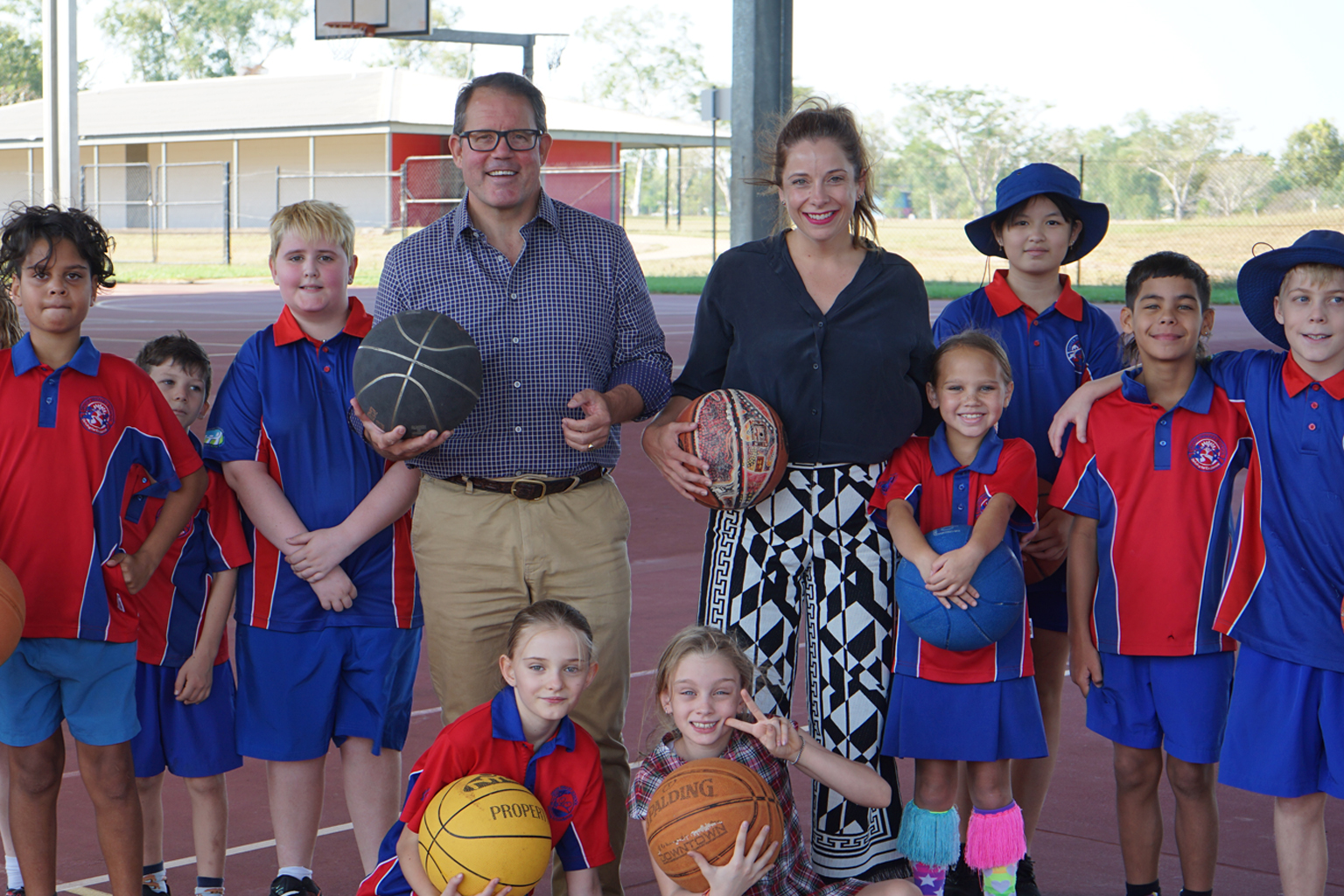 A group of children holding basketballs gathered on a court with MPs Luke Gosling and Anika Wells