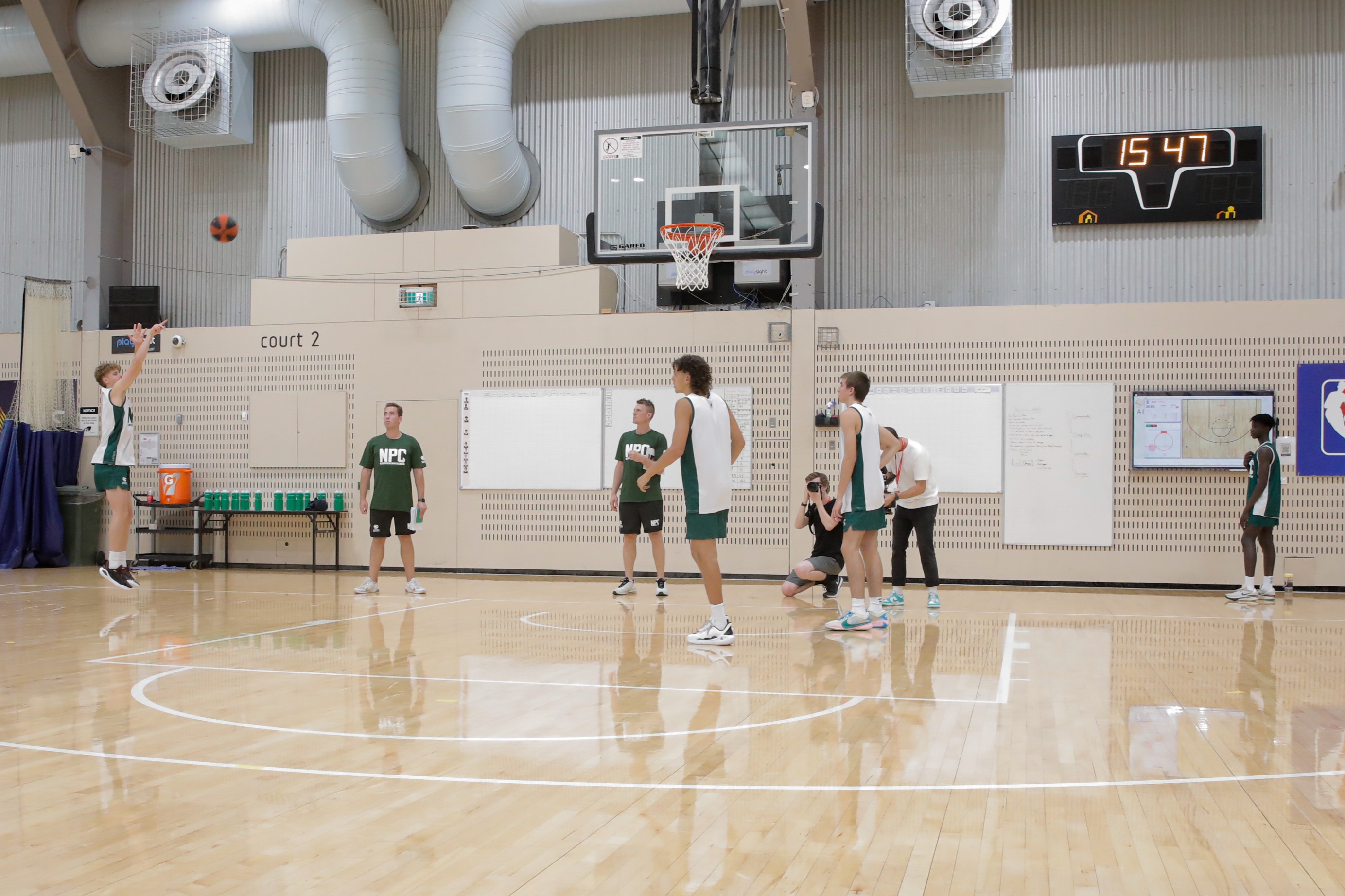 A group of teenage basketball athletes being coached during a shooting practice at the AIS basketball courts. 