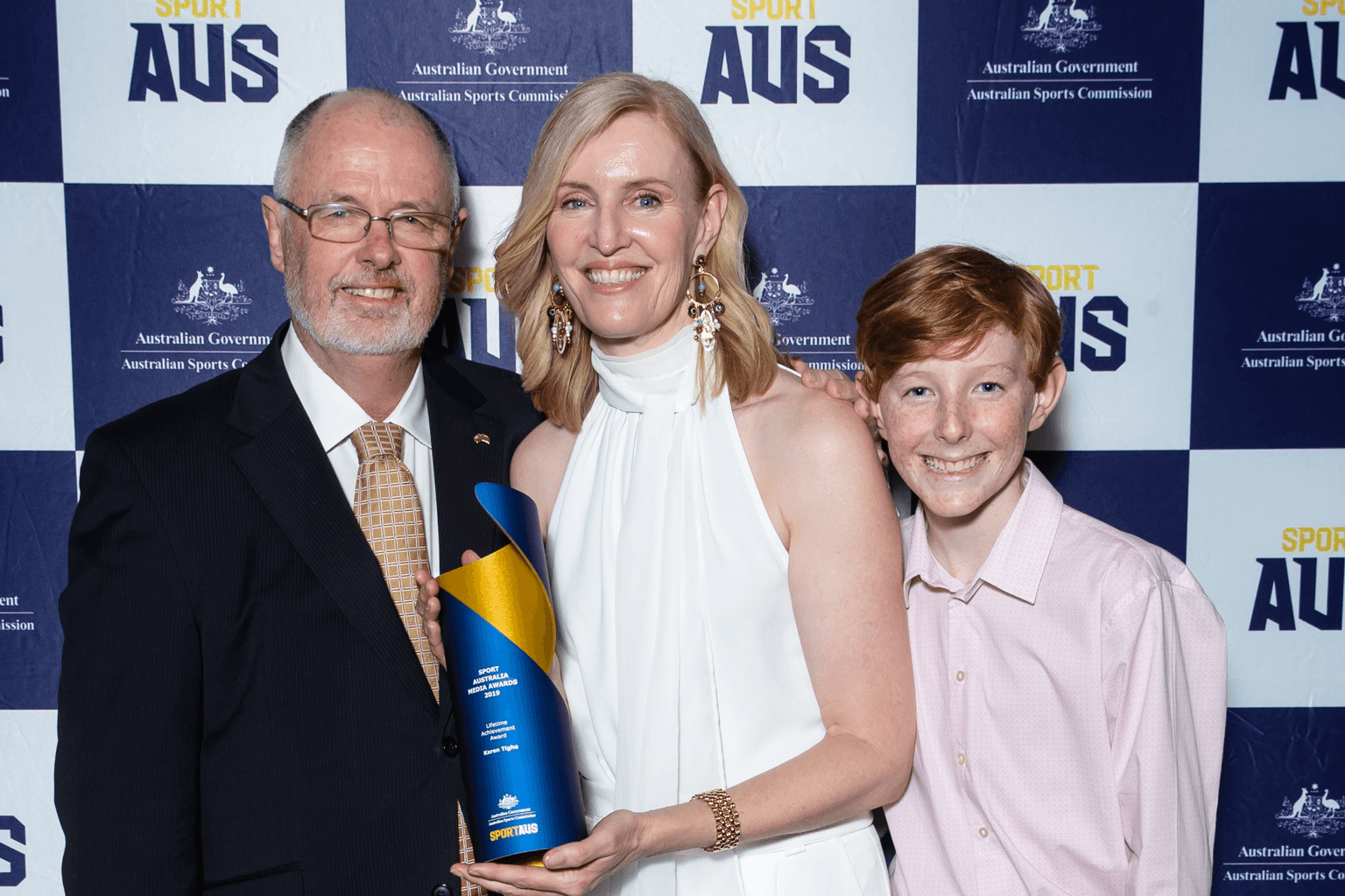 Karen Tighe, centre, holds her Sport Australia Media Awards lifetime achievement award trophy with husband Glenn Mitchell, left, and son.