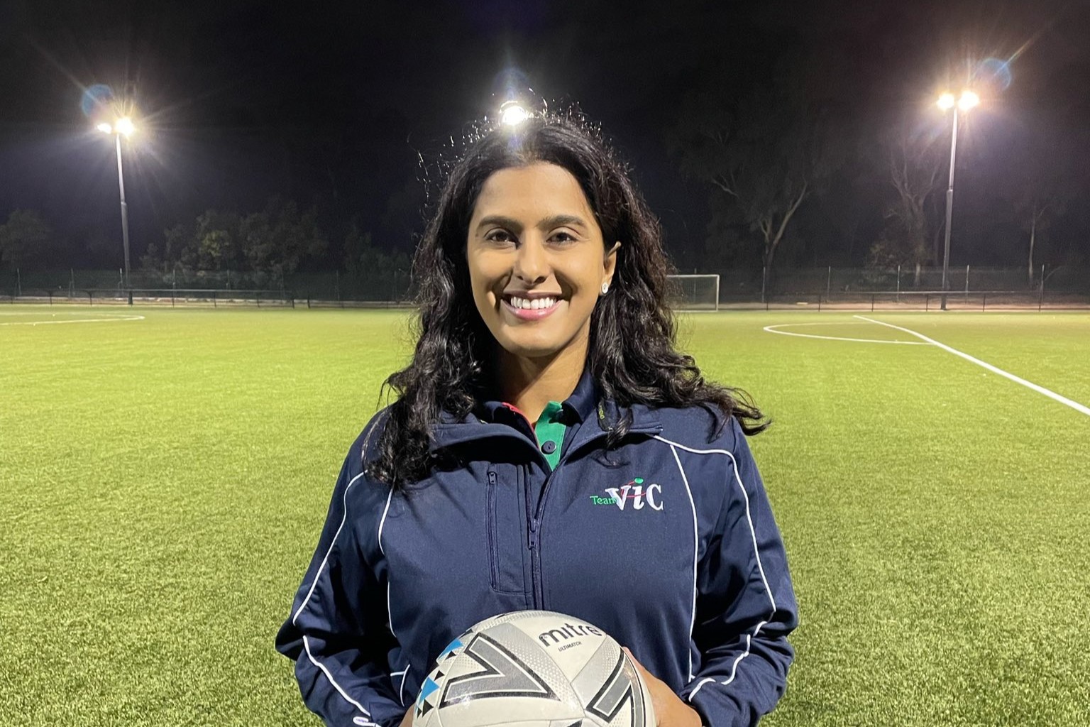 Aish Ravi in her role as state team coach for Victoria standing on a football field holding a soccer ball
