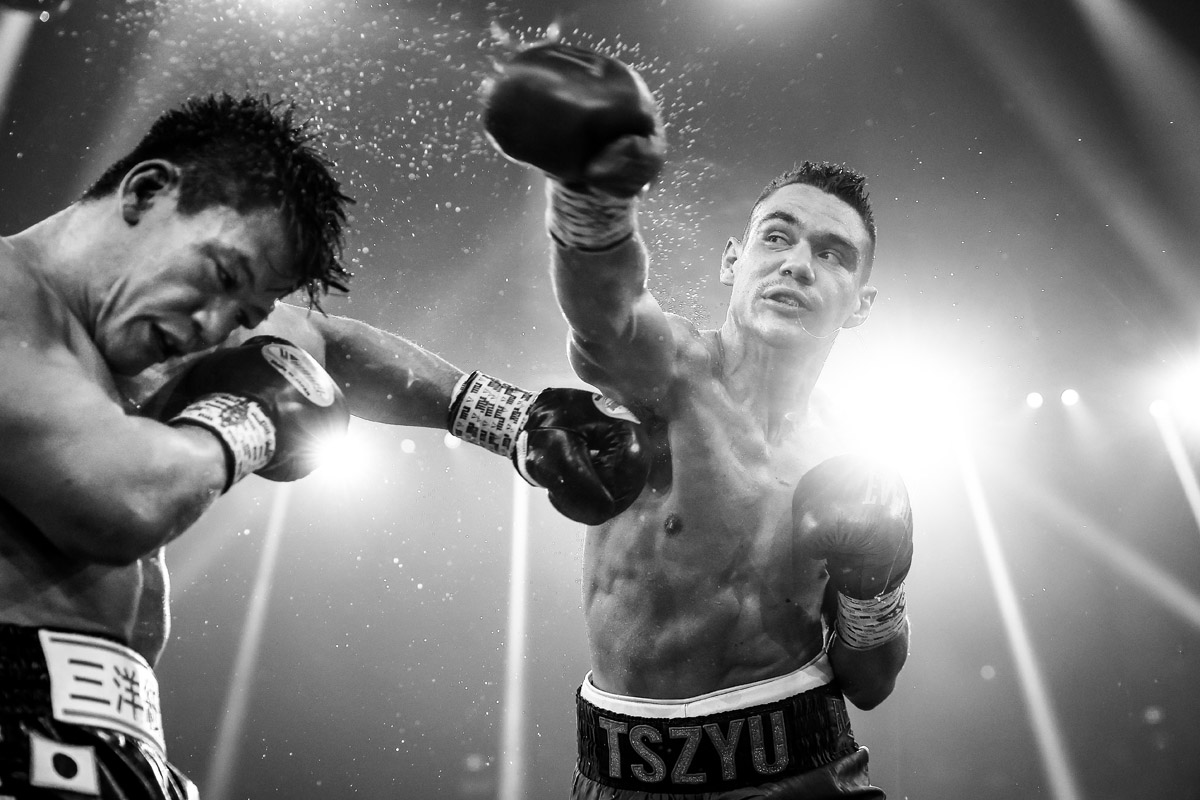 Black and white photo looking up at Tim Tszyu punching Takeshi Inoue. Water and sweat is spraying off Tszyu's glove and Takeshi's hair