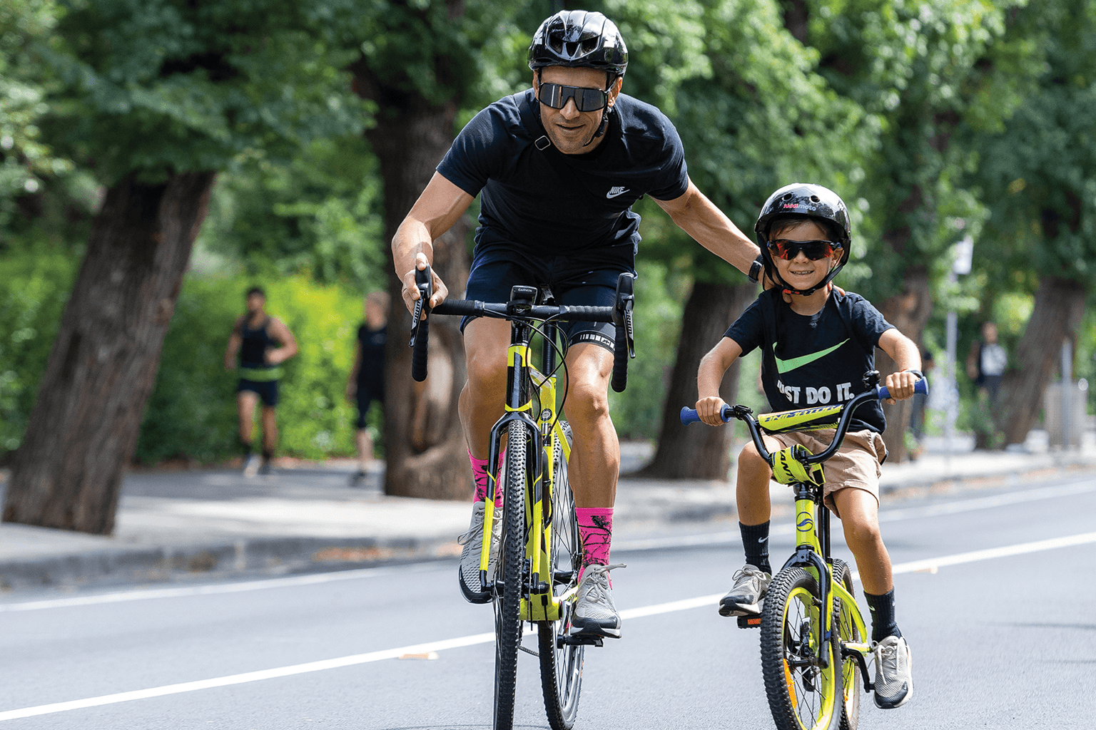 Adult male on road bike helps push a boy along on his bike
