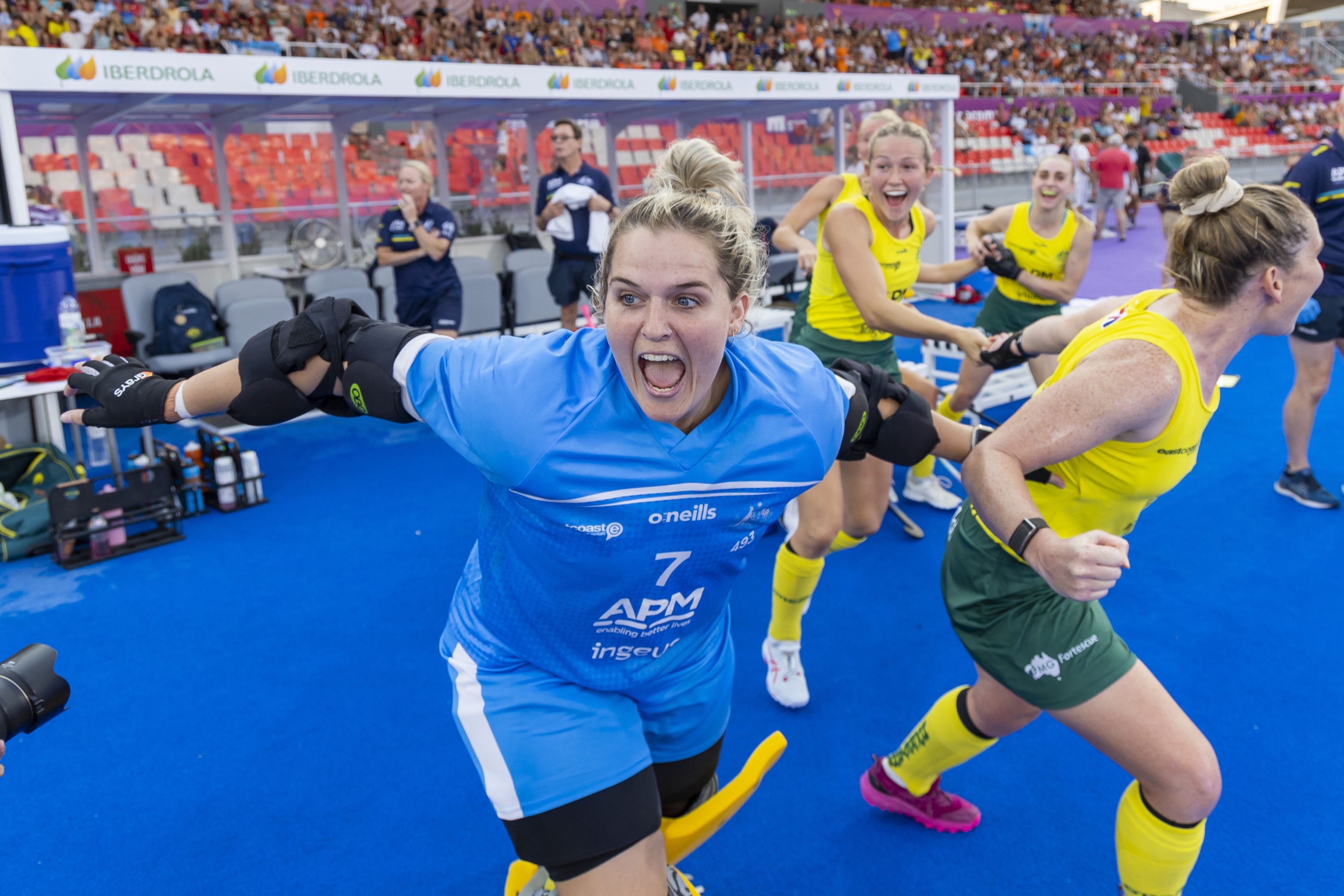 Aleisha Power in goalkeeper gear yells happily with team mates on sideline.