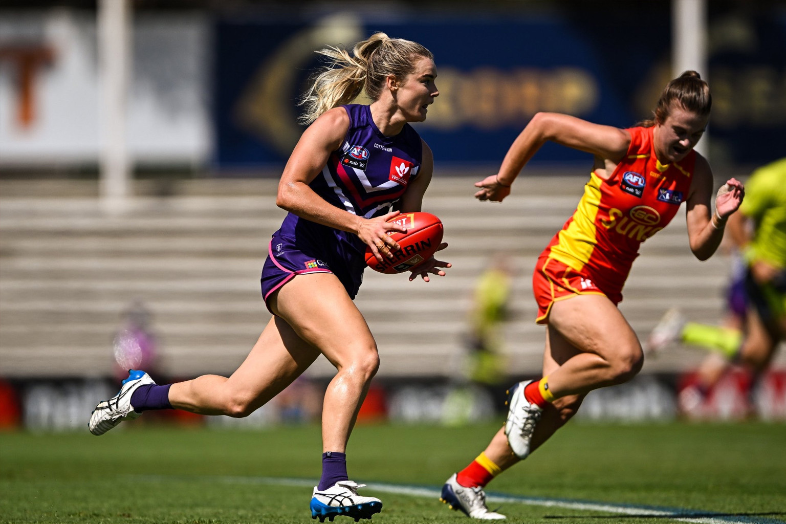 Hayley Miller playing with AFLW team Fremantle Dockers runs with the ball past a Gold Coast Suns player
