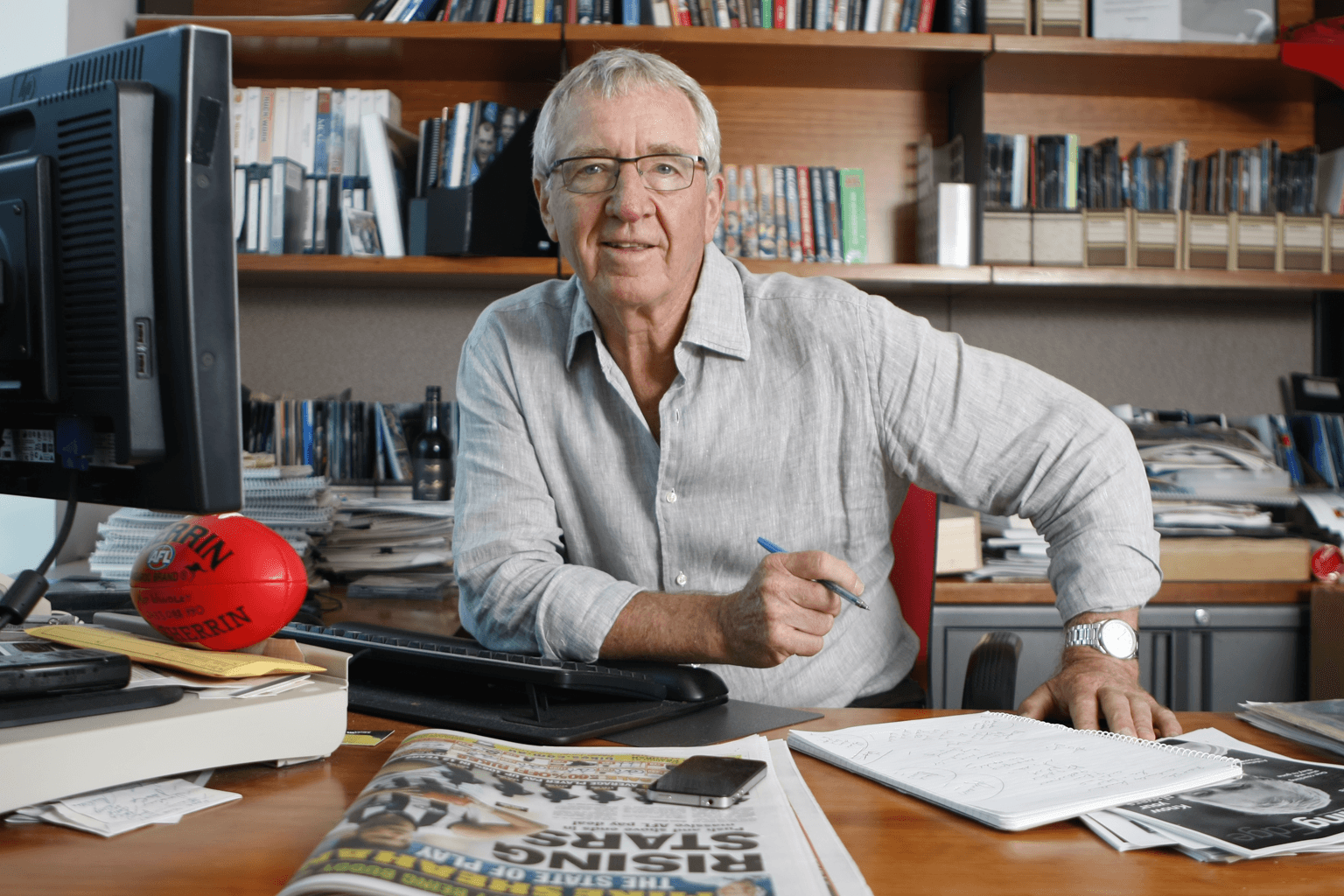 Mike Sheahan sits at his desk, behind a copies of the Herald Sun