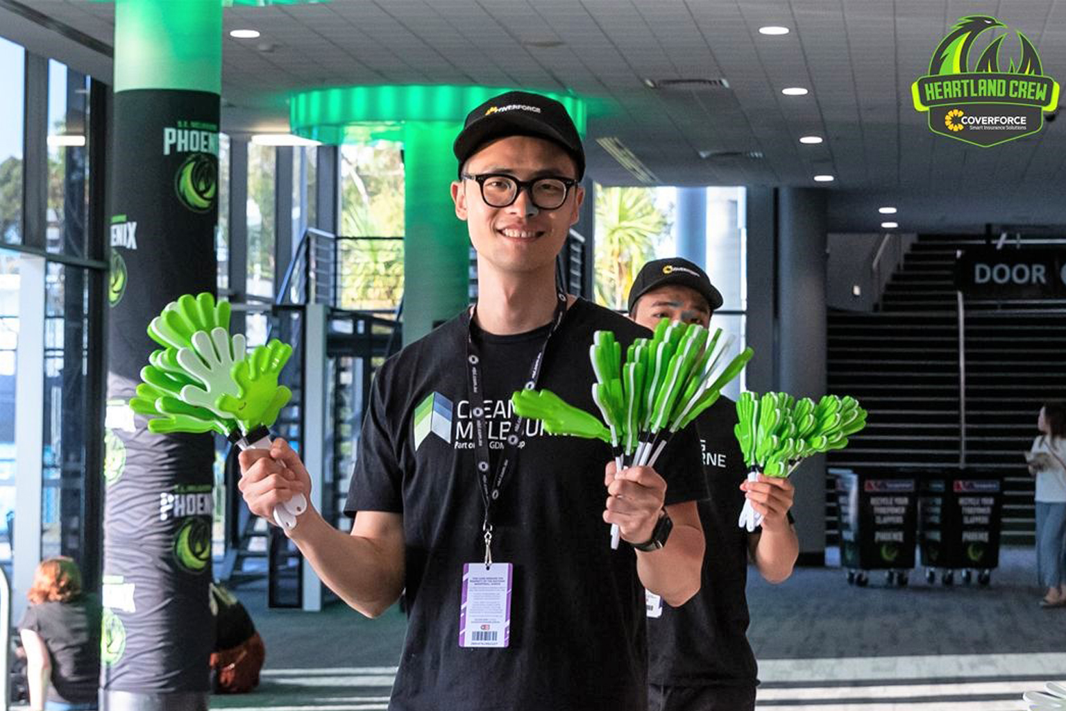 SEM Melbourne Phoenix volunteers stand in the stadium foyer holding plastic clapping hands to give to supporters.