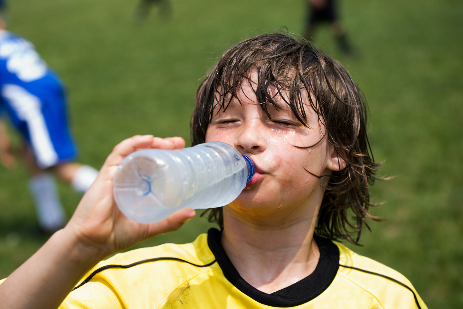 A boy with wet hair and face cools down with a drink of water.