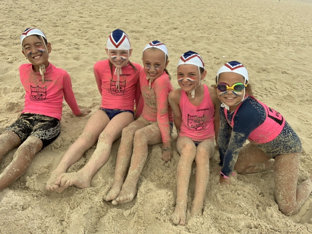 Group of young surf life savers sitting on the sand and smiling