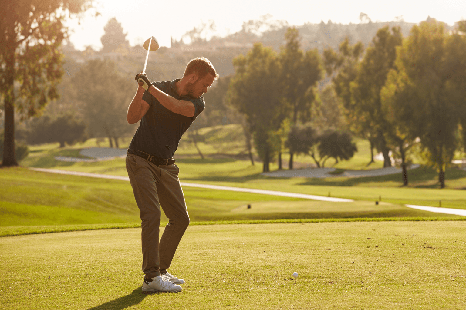 Man begins his swing to tee off on a golf course.