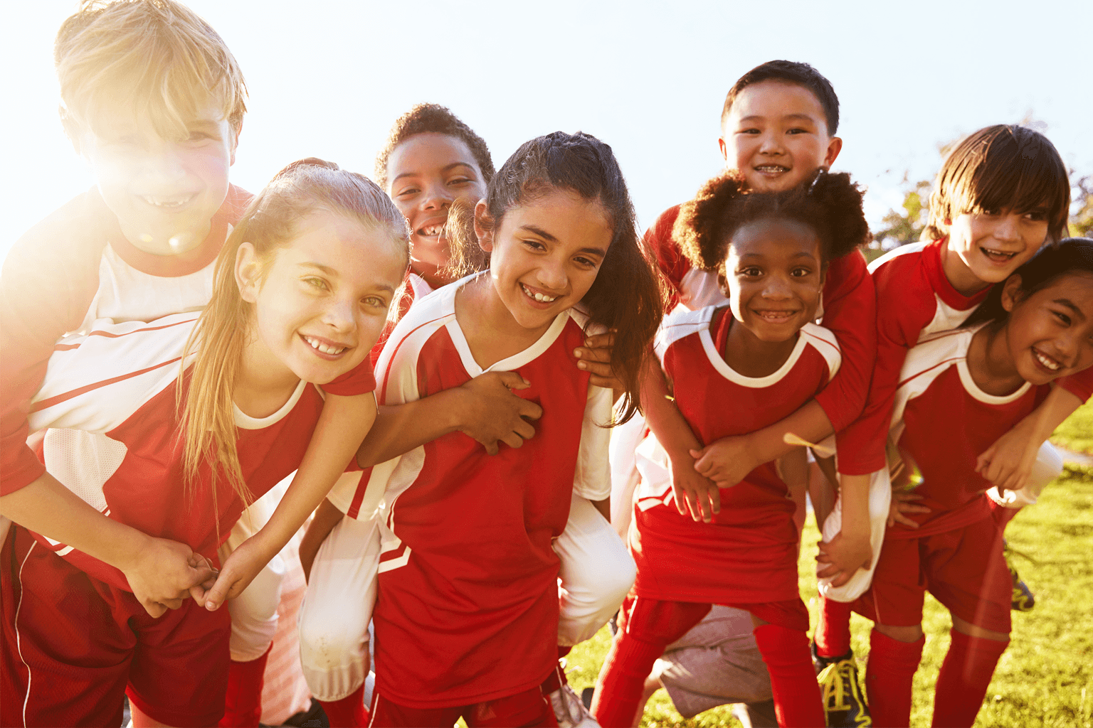 A group of children wearing football uniforms huddle while on the field.