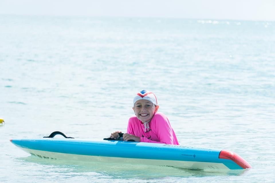 Young surf life saving participant leaning on a surf ski in the ocean and smiling